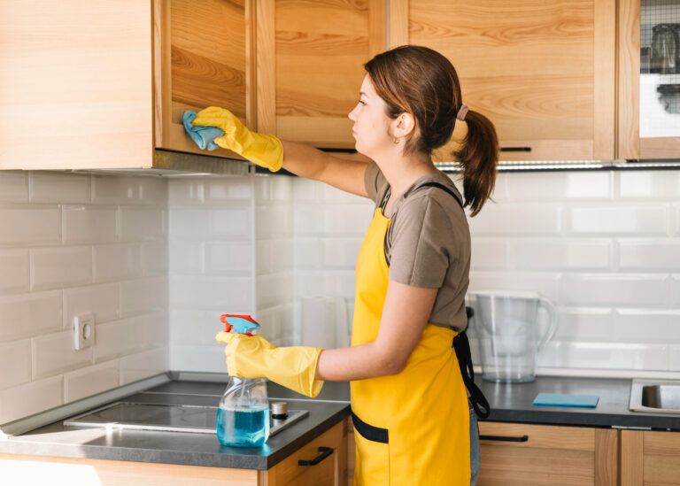 Woman cleaning kitchen cabinets with a spray bottle and cloth for a tidy and organized kitchen